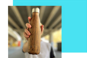 Miin Bottle drikkedunk i Teaktræ design holdt i hånden af en person med strakt arm under en bro